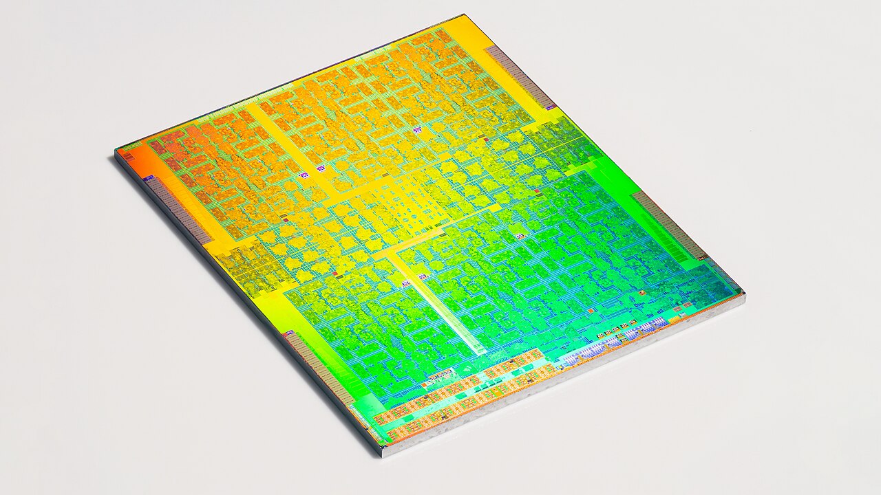 An exposed NVIDIA GP100 GPU die, photographed at an angle, with intricate gold, green and blue circuitry.